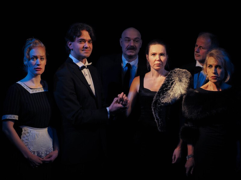 Sechs Personen in eleganter Kleidung stehen in einem dunklen Raum. Eine Frau tr&auml;gt eine Sch&uuml;rze, die anderen sind in Abendgarderobe gekleidet., &copy; Theater Atelier