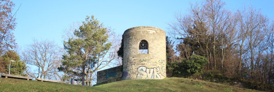 Eine alte, runde Ruine mit Graffiti steht auf einem grasbewachsenen Hügel, umgeben von kahlen Bäumen und blauem Himmel., © SMG