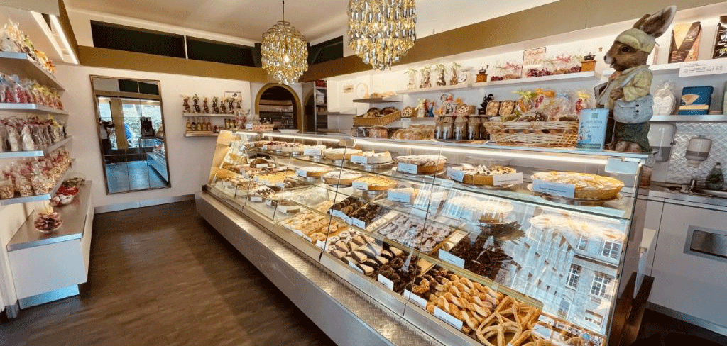 A cozy café with a display case full of pastries and chocolate. Decorative figurines and a chandelier complete the ambience., © FreCla Gastronomiebetriebe GmbH