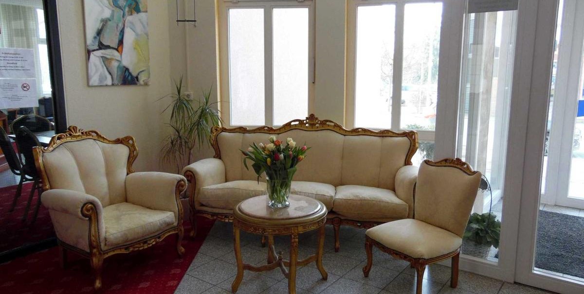 Elegant lobby with antique furniture: a sofa, two armchairs and a chair around a table with a bouquet of flowers. Artwork on the wall, large windows in the background., © Hotel Arcis