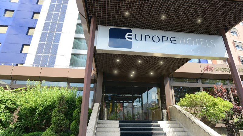 The entrance to a modern hotel with a sign reading “Europe Hotels Kongresshotel” above the stairs. Green bushes can be seen on the left., © Europe Hotels International The entrance to a modern hotel with a sign reading “Europe Hotels Kongresshotel” above the stairs. Green bushes can be seen on the left., © Europe Hotels International