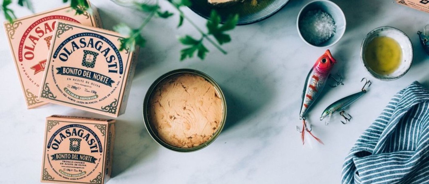 Olasagasti Thunfischdosen, Angelköder, Salz und Öl auf einem Tisch. Ein blau-weiß gestreiftes Tuch liegt daneben., © Sardinen und Feinkost, Stuttgart