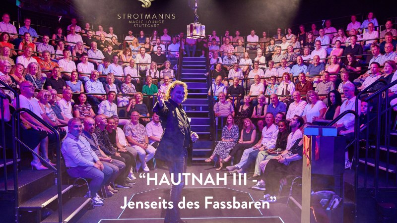 Ein Magier performt vor einem vollen Publikum in der Strotmanns Magic Lounge Stuttgart. Der Raum ist stimmungsvoll beleuchtet., © Strotmanns Magic Lounge Ein Magier performt vor einem vollen Publikum in der Strotmanns Magic Lounge Stuttgart. Der Raum ist stimmungsvoll beleuchtet., © Strotmanns Magic Lounge