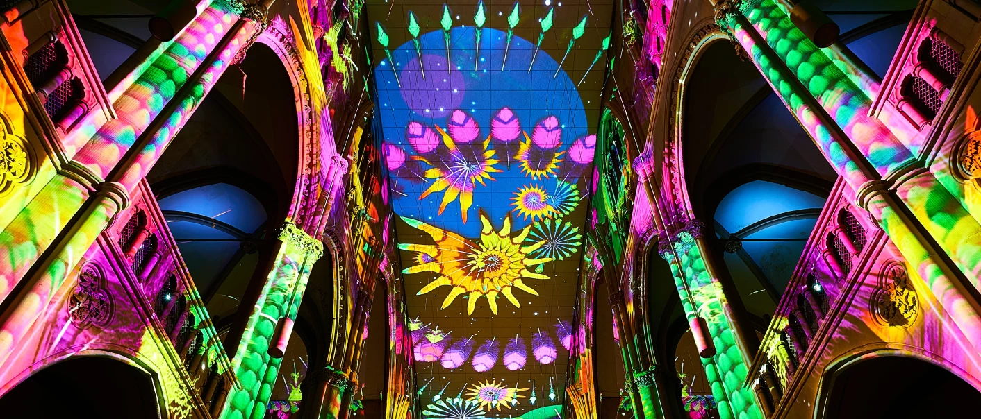 Colorful light projections inside Stuttgart's Johanneskirche, featuring floral patterns on the vaults and ceiling., © Andreas Kaiser Colorful light projections inside Stuttgart's Johanneskirche, featuring floral patterns on the vaults and ceiling., © Andreas Kaiser