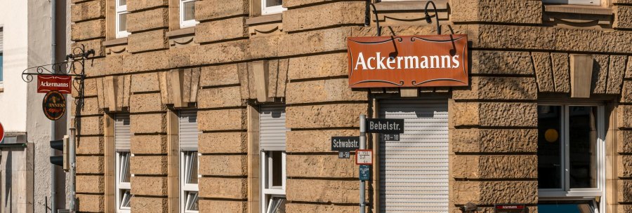 Corner building with the sign 'Ackermanns' on the facade. Street signs for Bebelstr. and Schwabstr. are visible, as are several advertising posters., &copy; SMG Stuttgart Marketing GmbH - Sarah Schmid