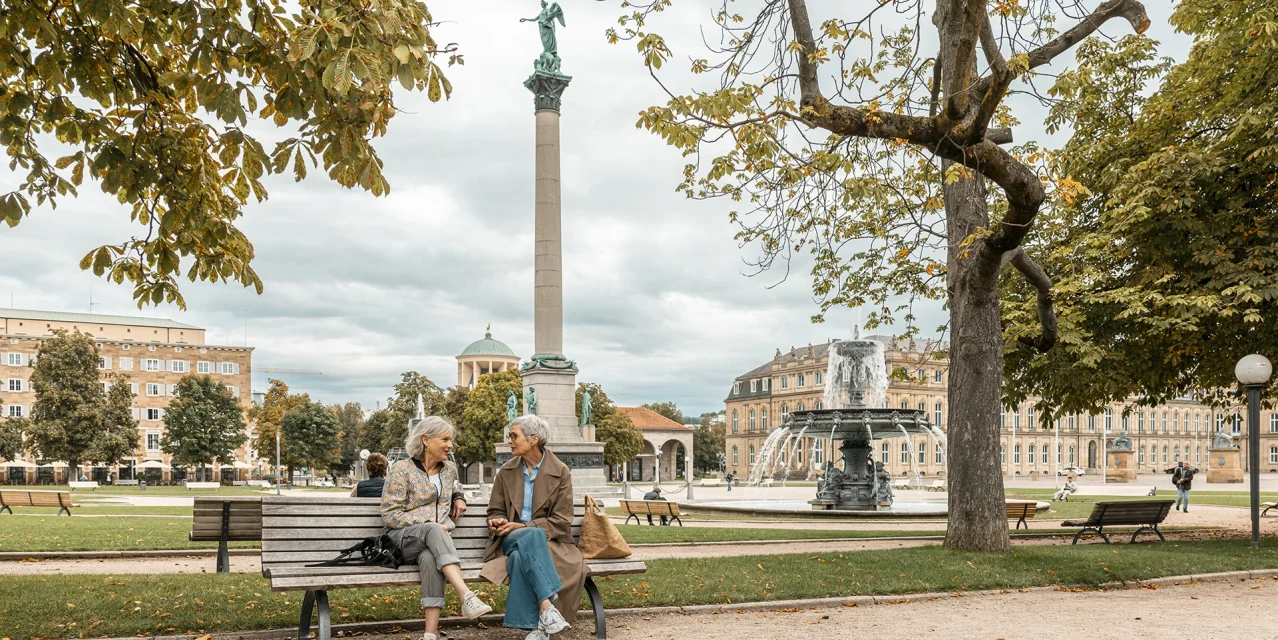 Zwei Frauen sitzen auf einer Bank am Schlossplatz in Stuttgart, im Hintergrund Jubiläumssäule, Brunnen und historische Gebäude., © SMG, Sarah Schmid Zwei Frauen sitzen auf einer Bank am Schlossplatz in Stuttgart, im Hintergrund Jubiläumssäule, Brunnen und historische Gebäude., © SMG, Sarah Schmid