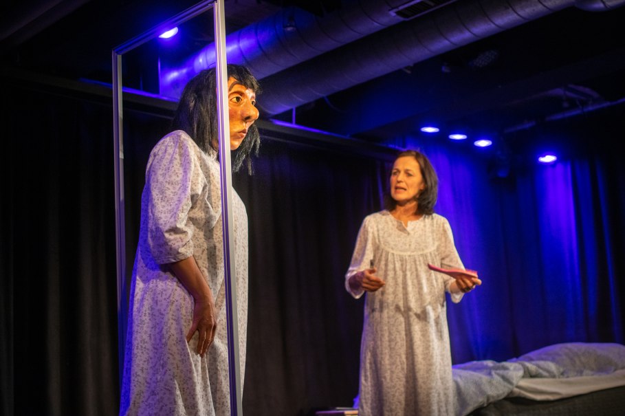 Zwei Personen in Nachthemden auf einer B&uuml;hne. Eine tr&auml;gt eine gro&szlig;e Maske, die andere h&auml;lt ein Buch. Die Szene ist in blauem Licht beleuchtet., &copy; Improtheater Stuttgart