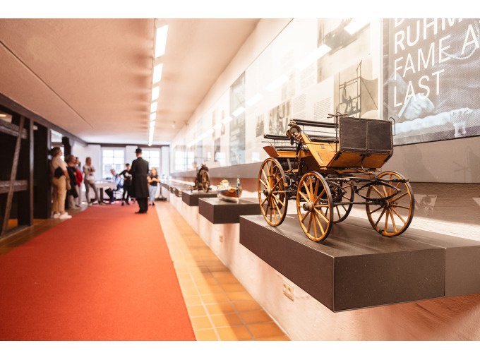 Ein historisches Fahrzeugmodell in einem Museum. Besucher betrachten die Ausstellung entlang eines roten Teppichs., © Eigenbetrieb Tourismus und Citymanagement Schorndorf Ein historisches Fahrzeugmodell in einem Museum. Besucher betrachten die Ausstellung entlang eines roten Teppichs., © Eigenbetrieb Tourismus und Citymanagement Schorndorf