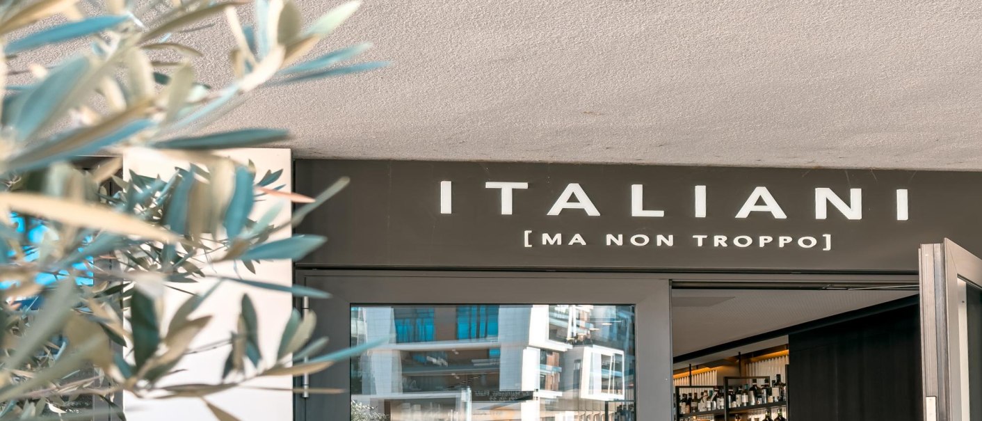 Entrance to a restaurant with the sign 'ITALIANI [MA NON TROPPO]'. Blurred plants can be seen in the foreground., &copy; SMG Stuttgart Marketing GmbH - Sarah Schmid