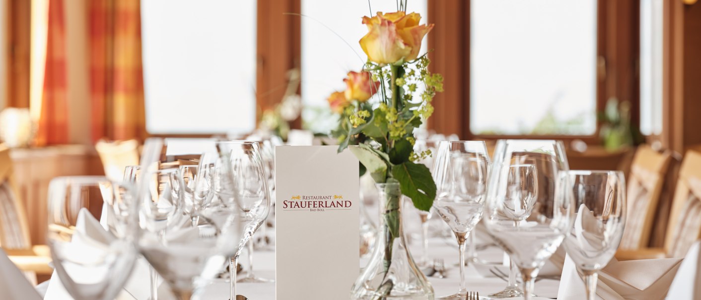 Eleganter Tisch im Badhotel Restaurant Stauferland, gedeckt mit Gläsern, Besteck und Blumen. Im Hintergrund große Fenster mit Vorhängen., © Badhotel Restaurant Stauferland