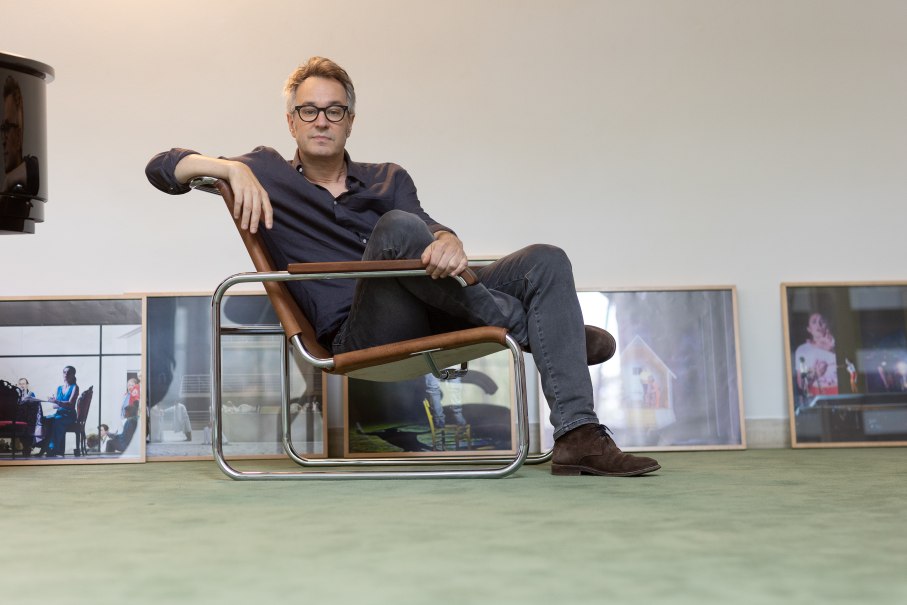 Eine Person sitzt entspannt in einem modernen Stuhl. Im Hintergrund stehen gerahmte Bilder auf dem Boden. Die Atmosph&auml;re wirkt k&uuml;nstlerisch und gelassen., &copy; Alberto Novelli