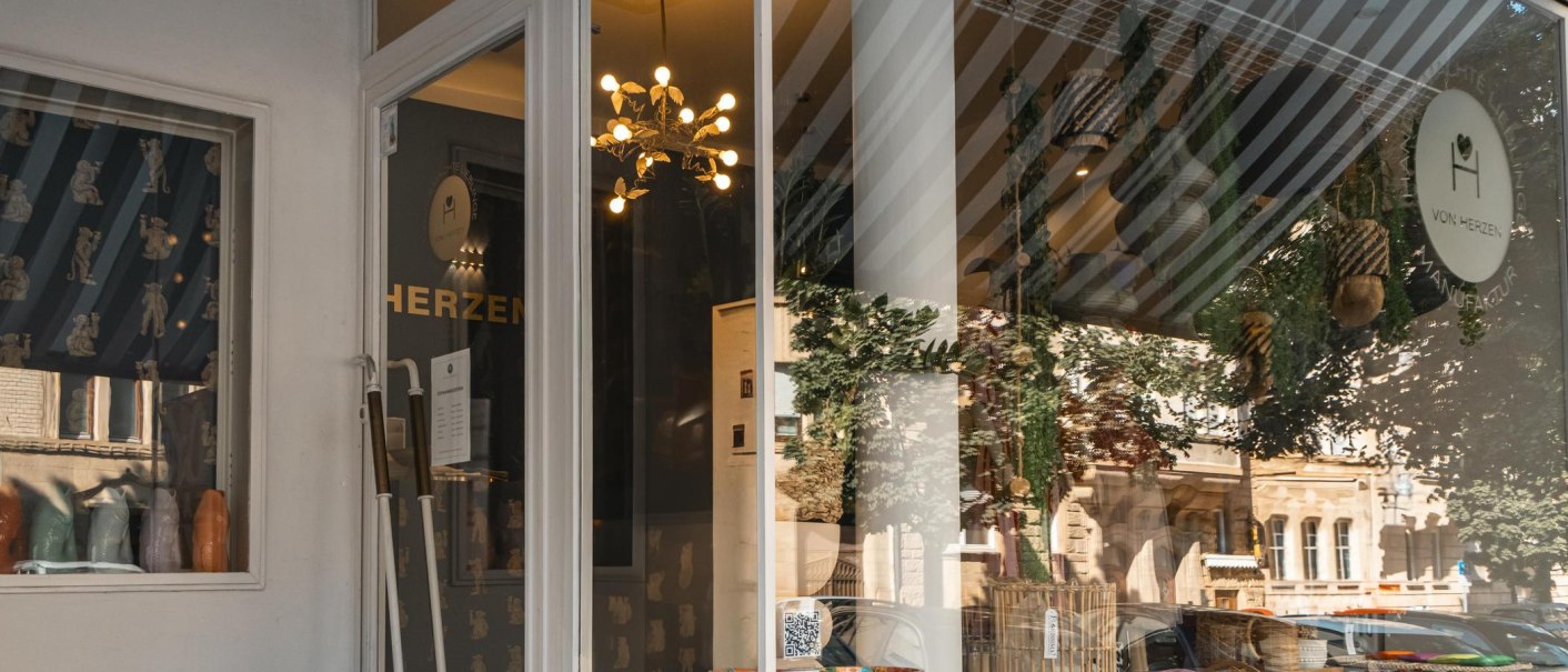 Schaufenster eines Geschäfts namens 'Von Herzen', dekoriert mit Pflanzen, Lampen und Körben. Die Spiegelung zeigt eine Straße mit Gebäuden., © SMG, Sarah Schmid
