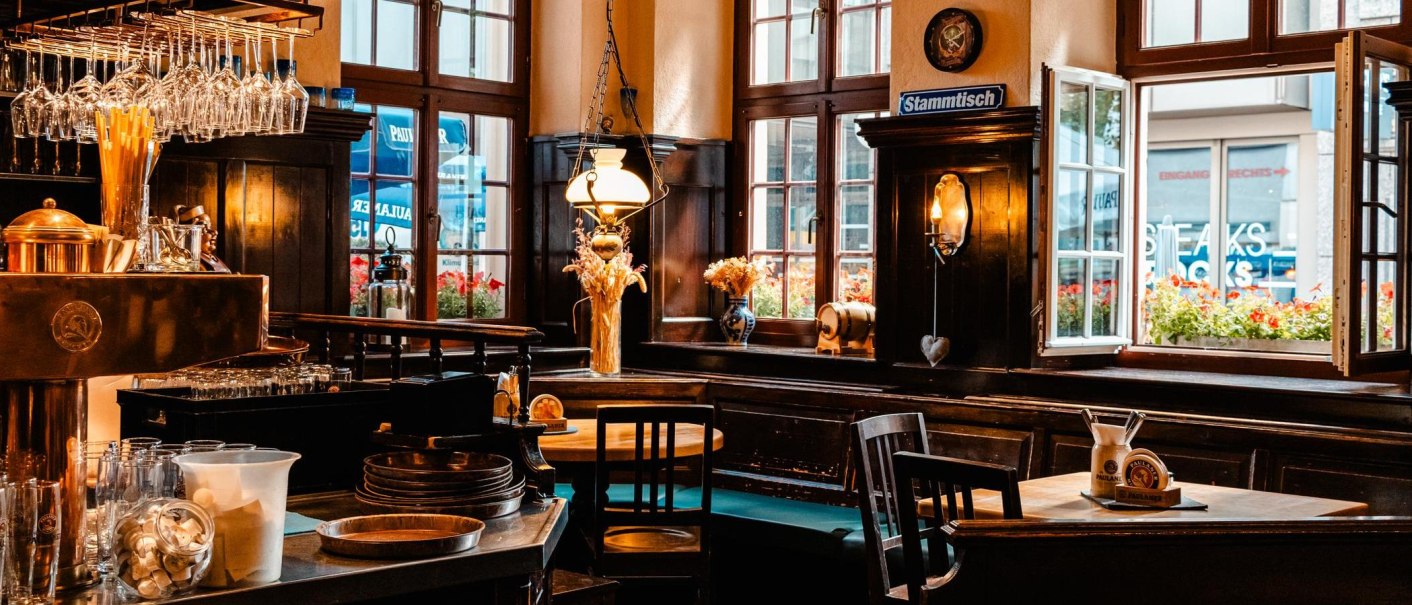 Gem&uuml;tlicher Innenraum eines Paulaner-Restaurants mit Holzm&ouml;beln, Bar, Gl&auml;sern und Dekorationen. Offene Fenster mit Blick nach drau&szlig;en., &copy; Stuttgart Marketing GmbH, Sarah Schmid