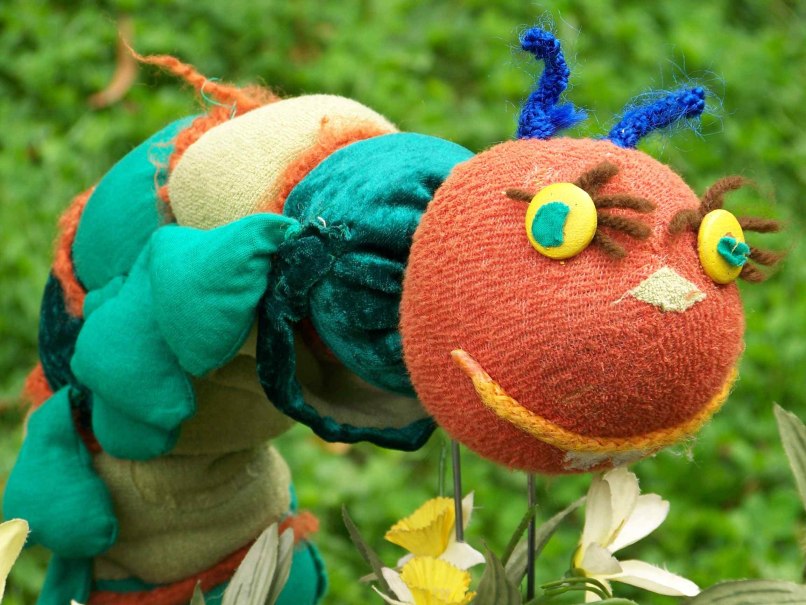 Bunte Stoffraupe mit rotem Kopf, gelben Augen und blauen Fühlern vor grünem Hintergrund. Sie wirkt fröhlich und kindgerecht gestaltet., © Nellys Puppentheater Bunte Stoffraupe mit rotem Kopf, gelben Augen und blauen Fühlern vor grünem Hintergrund. Sie wirkt fröhlich und kindgerecht gestaltet., © Nellys Puppentheater