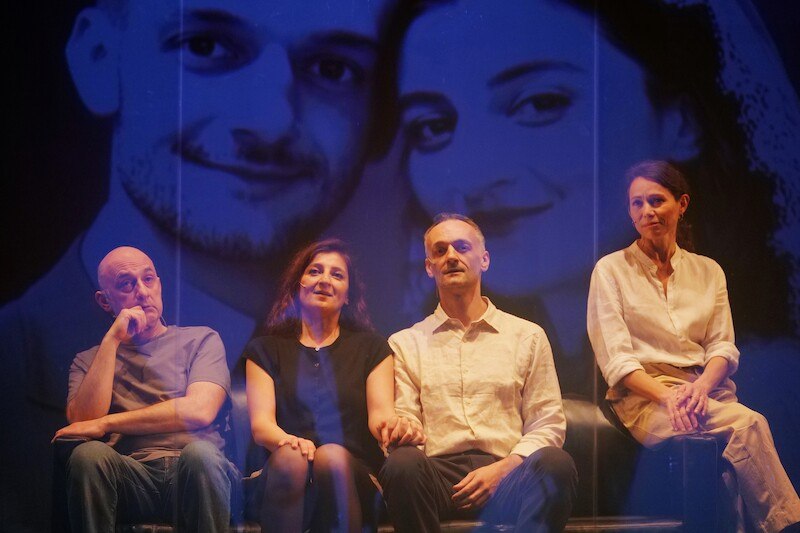 Vier Personen sitzen auf einer Bühne, im Hintergrund ein großes, unscharfes Porträt eines Paares. Der Titel des Bildes ist 'Illusionen'., © tri-bühne e.V. Vier Personen sitzen auf einer Bühne, im Hintergrund ein großes, unscharfes Porträt eines Paares. Der Titel des Bildes ist 'Illusionen'., © tri-bühne e.V.