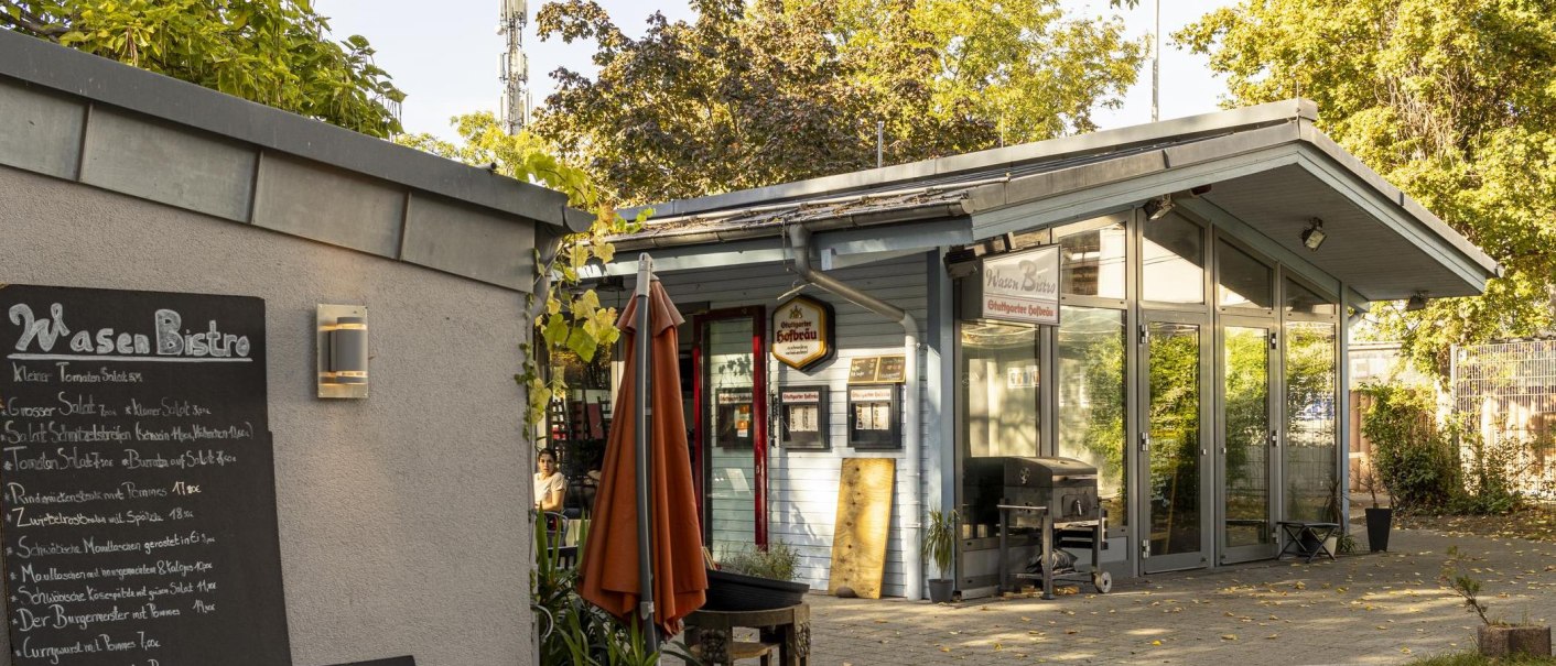 Ein kleines Bistro mit Glasfront und Men&uuml;tafel. Ein Sonnenschirm steht davor, umgeben von B&auml;umen und Pflanzen., &copy; Stuttgart-Marketing GmbH, Sarah Schmid