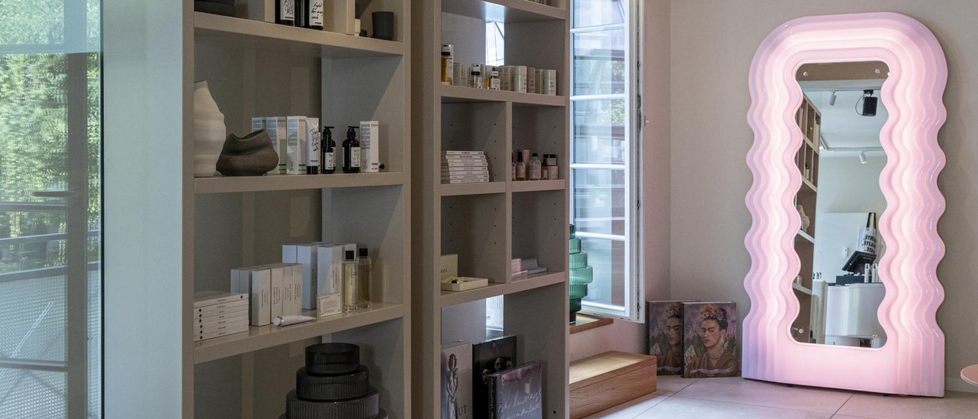Shelves with cosmetic products, next to a large, wave-shaped mirror with pink lighting. In the background is a window with a view outside., © SMG Stuttgart Marketing GmbH - Sarah Schmid