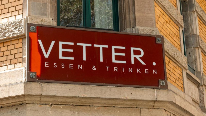 Rotes Schild mit der Aufschrift 'Vetter. Essen & Trinken' an einer Gebäudeecke aus gelben Ziegeln., © SMG, Sarah Schmid