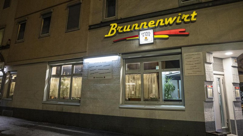 Das Restaurant Brunnenwirt bei Nacht, beleuchtet mit gelbem Schriftzug. Ein Mann steht an einem Tisch vor dem Eingang., © SMG, Sarah Schmid