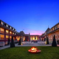 The Waldhotel Stuttgart at dusk, with illuminated windows and a fireplace in the garden. The sky is blue with a pink stripe., © Waldhotel Stuttgart GmbH The Waldhotel Stuttgart at dusk, with illuminated windows and a fireplace in the garden. The sky is blue with a pink stripe., © Waldhotel Stuttgart GmbH