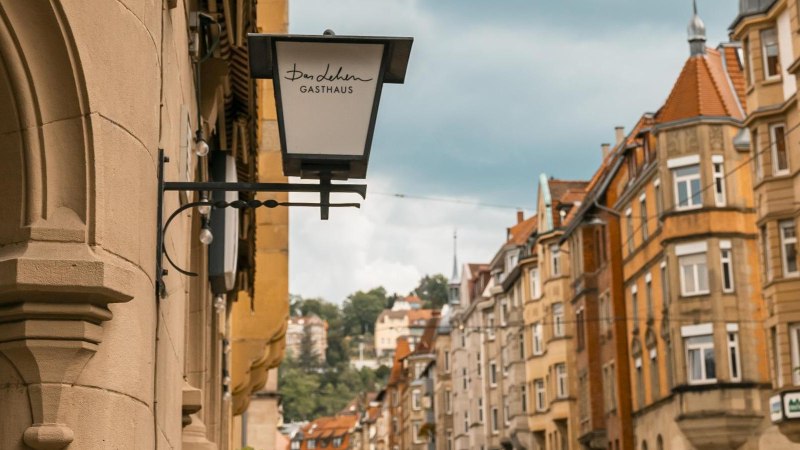 Straßenszene in Stuttgart mit einem Gasthausschild "Das Lehen" und historischen Gebäuden im Hintergrund., © SMG, Sarah Schmid Straßenszene in Stuttgart mit einem Gasthausschild "Das Lehen" und historischen Gebäuden im Hintergrund., © SMG, Sarah Schmid