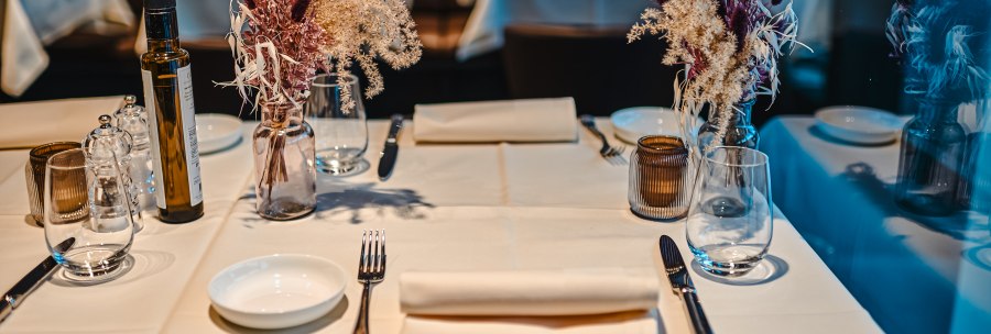 An elegantly laid table in a restaurant with white tablecloths, flower arrangements, glasses and cutlery., © Feinkost Böhm GmbH An elegantly laid table in a restaurant with white tablecloths, flower arrangements, glasses and cutlery., © Feinkost Böhm GmbH