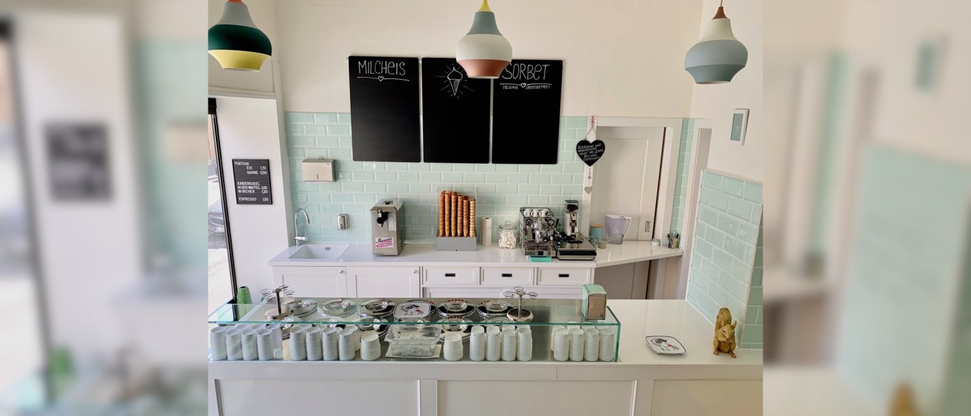 Eisdiele mit Theke, Eismaschine, Kaffeebereiter und Eiswaffeln. Pastellfarbene Fliesen und Lampen. Schwarze Tafeln mit Eisangeboten., &copy; Zur Schleckerei