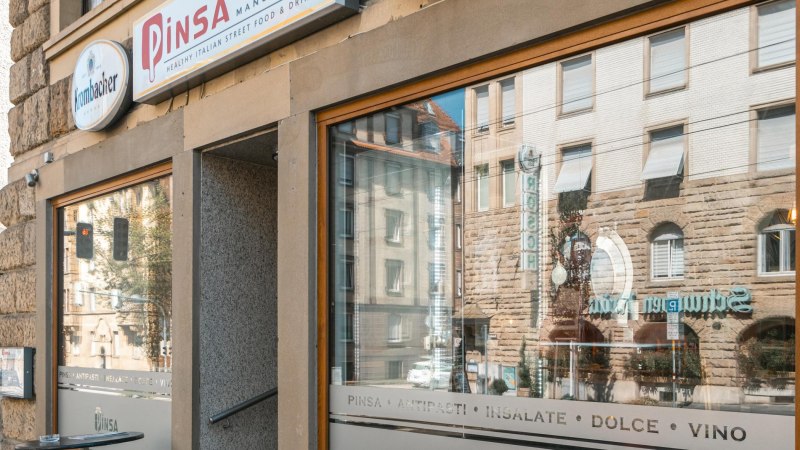 Exterior view of a restaurant with the inscription 'Pinsa Manufaktur' and reflection of buildings in the window., © SMG Stuttgart Marketing GmbH - Sarah Schmid