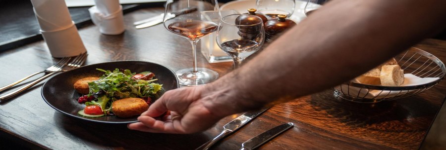 Ein Teller mit Salat und Kroketten wird auf einem gedeckten Tisch in einem Restaurant serviert. Im Hintergrund stehen Weingl&auml;ser und ein Brotkorb., &copy; Stuttgart-Marketing GmbH, Martina Denker