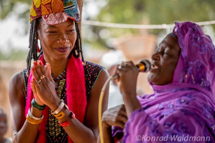 Zwei Frauen, eine klatscht, die andere singt in ein Mikrofon, beide in bunter Kleidung., © Beetz Brothers