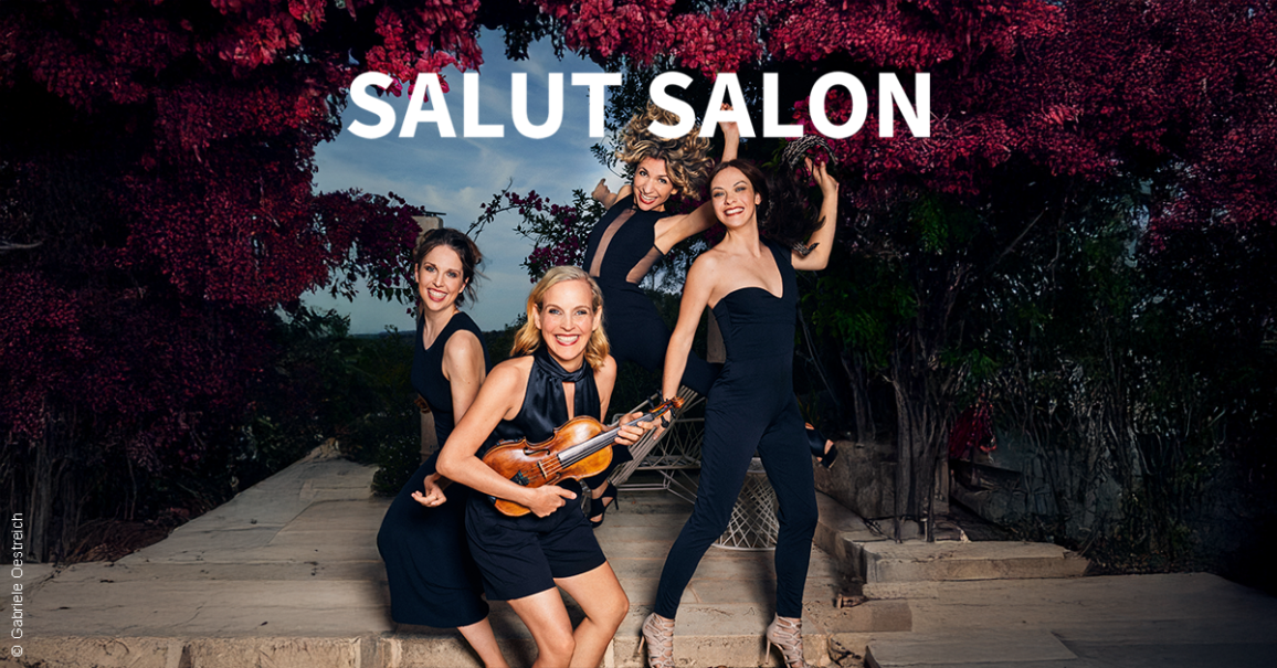 Vier Frauen in schwarzen Outfits posieren fröhlich mit einer Geige vor einer blühenden Kulisse. Oben steht der Schriftzug 'Salut Salon'., © links im Bild Vier Frauen in schwarzen Outfits posieren fröhlich mit einer Geige vor einer blühenden Kulisse. Oben steht der Schriftzug 'Salut Salon'., © links im Bild