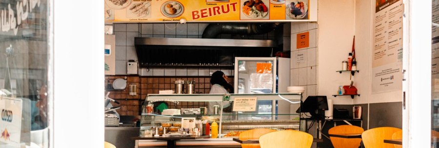 A snack bar with a yellow 'Imbiss Beirut' sign, empty tables and a person behind the counter., &copy; Stuttgart Marketing GmbH, Sarah Schmid