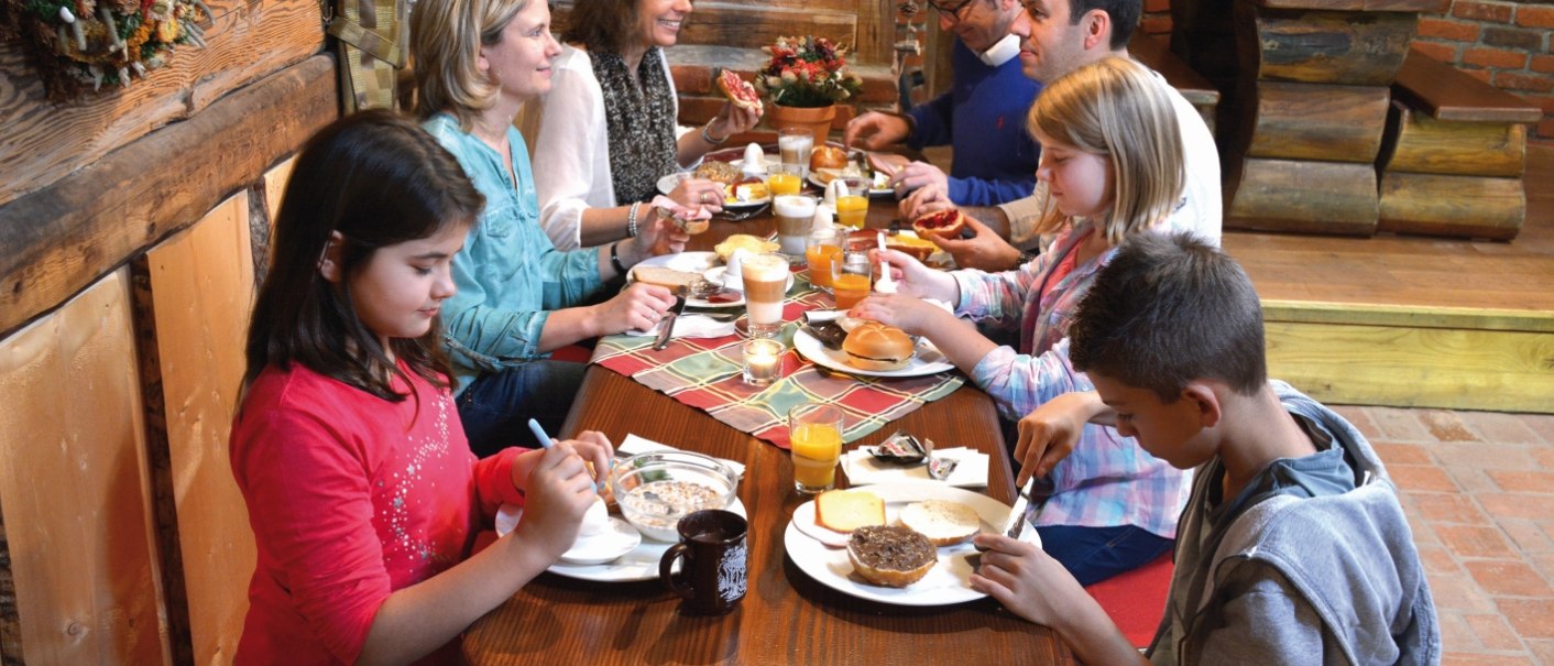 People are having breakfast at a wooden table in a cozy, rustic setting. They're having coffee, juice, and rolls., &copy; Tripsdrill Natur-Resort GmbH