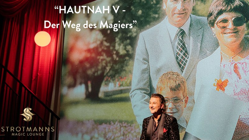A magician stands in front of a large family photo, entitled 'HAUTNAH V - Der Weg des Magiers'. Stage with red curtain, logo of Strotmann's Magic Lounge., &copy; Strotmanns Magic Lounge