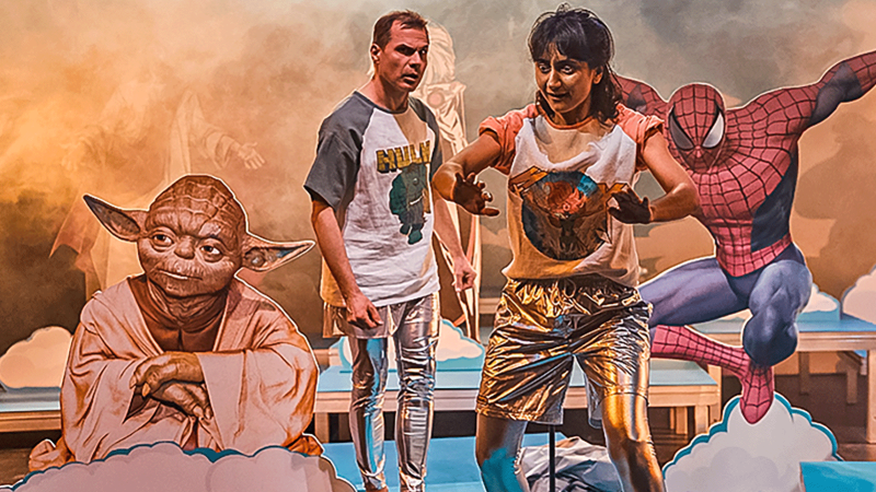 Two people on a stage with Yoda, Spider-Man and Wonder Woman in the background. The scene looks imaginative and colorful., © JES, Alex Wunsch
