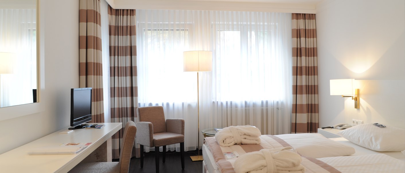 Bright double room with modern design, double bed, desk, TV and armchair. Large windows with striped curtains., &copy; relexa Waldhotel Schatten