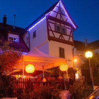 An illuminated half-timbered house with a white tent in the garden. Colorful lanterns and fairy lights create a cozy atmosphere at night., © Weingut Ruoff An illuminated half-timbered house with a white tent in the garden. Colorful lanterns and fairy lights create a cozy atmosphere at night., © Weingut Ruoff