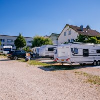 Wohnmobilstellplatz mit Wohnwagen und Autos, umgeben von Gebäuden und Bäumen unter klarem Himmel., © Stuttgart-Marketing GmbH, Thomas Niedermüller Wohnmobilstellplatz mit Wohnwagen und Autos, umgeben von Gebäuden und Bäumen unter klarem Himmel., © Stuttgart-Marketing GmbH, Thomas Niedermüller