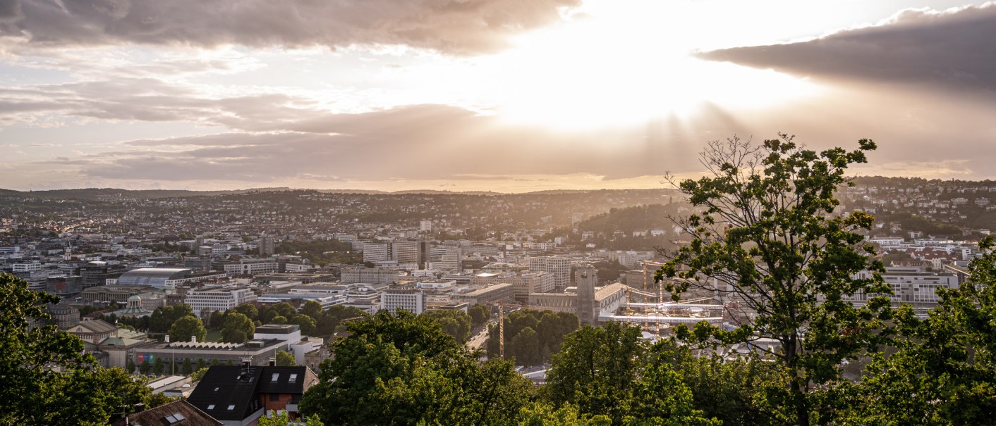 Blick von der Uhlandshöhe auf Stuttgart bei Sonnenuntergang. Die Stadt liegt unter einem dramatischen Himmel mit Sonnenstrahlen und Wolken., © Christine Garcia, Urban Trickytine