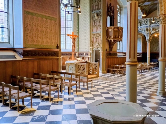 Die Schlosskirche Stuttgart zeigt eine elegante Innenansicht mit Holzb&auml;nken, einem Kruzifix und einer kunstvoll geschnitzten Kanzel auf einem schwarz-wei&szlig;en Boden., &copy; Stiftsmusik Stuttgart