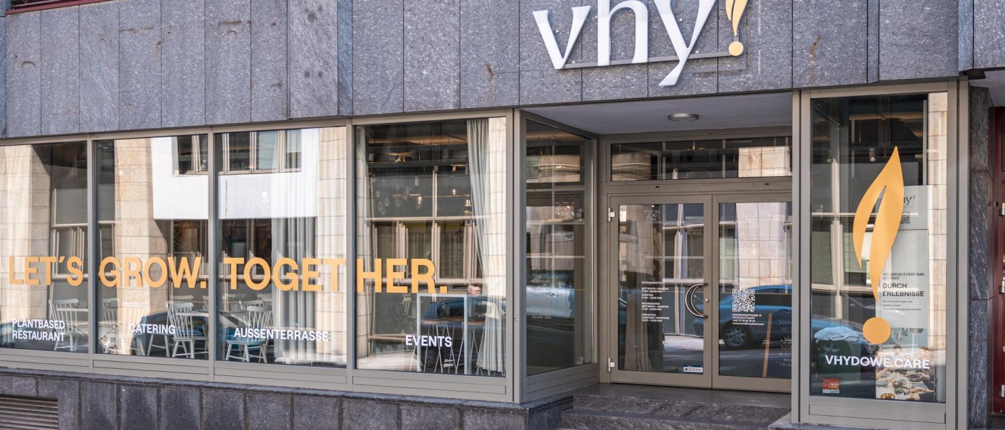 Eingang eines Restaurants mit der Aufschrift 'vhy!' und großen Fenstern. Schriftzug 'LET'S GROW. TOGETHER.' auf den Fenstern., © SMG, Sarah Schmid