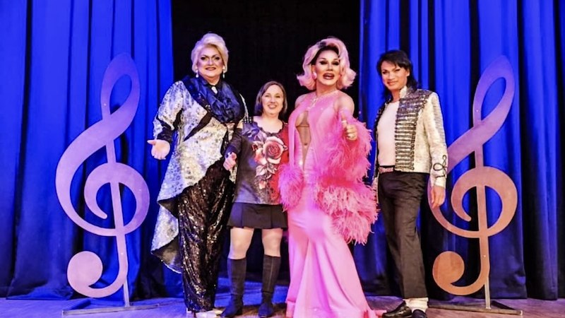 Vier Personen posieren auf einer Bühne mit blauen Vorhängen und großen Notenschlüssel-Dekorationen. Sie tragen auffällige Kostüme., © Tanja Silzer Events Vier Personen posieren auf einer Bühne mit blauen Vorhängen und großen Notenschlüssel-Dekorationen. Sie tragen auffällige Kostüme., © Tanja Silzer Events