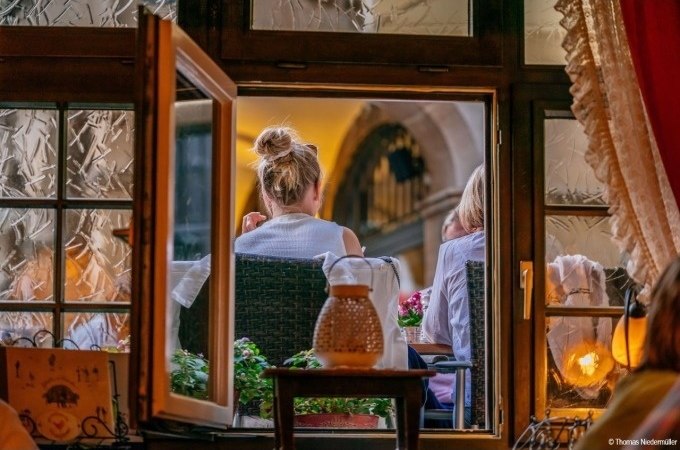 Blick durch ein offenes Fenster auf zwei Personen, die in einem gemütlichen Restaurant sitzen. Warme Beleuchtung und Dekorationen sind sichtbar., © Stuttgart Marketing GmbH