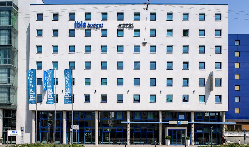 The ibis budget hotel in Stuttgart City Nord has a white façade with blue windows and signs. Hotel flags fly in front of the building., © ibis budget Stuttgart City Nord The ibis budget hotel in Stuttgart City Nord has a white façade with blue windows and signs. Hotel flags fly in front of the building., © ibis budget Stuttgart City Nord