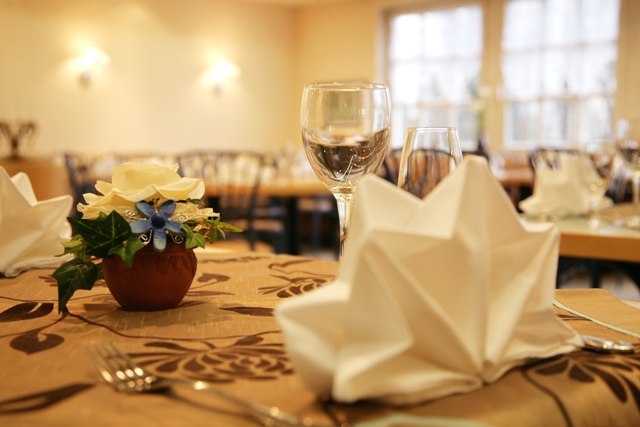 An elegantly set table in a restaurant with a folded napkin, a wine glass, and a floral arrangement., © ateckhotel An elegantly set table in a restaurant with a folded napkin, a wine glass, and a floral arrangement., © ateckhotel