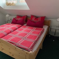 Gemütliches Schlafzimmer mit einem Holzbett, roten karierten Bettbezügen und zwei Nachttischen unter einem Dachfenster., © Weinhof am Württemberg