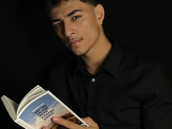 Ein Mann in schwarzem Hemd liest ein Buch mit dem Titel 'Der Tag, an dem meine Kindheit endete' vor schwarzem Hintergrund., © Theater Atelier Ein Mann in schwarzem Hemd liest ein Buch mit dem Titel 'Der Tag, an dem meine Kindheit endete' vor schwarzem Hintergrund., © Theater Atelier