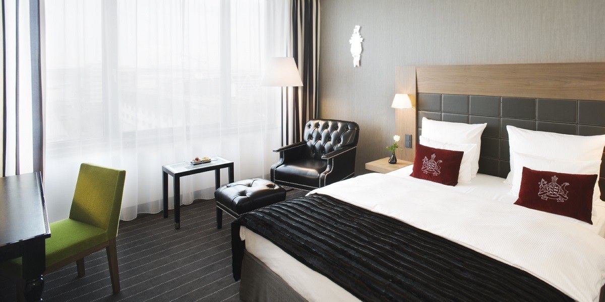 Elegantes Hotelzimmer mit großem Bett, Ledersessel, grünem Stuhl und Tisch am Fenster., © Mövenpick Hotel Stuttgart Airport Elegantes Hotelzimmer mit großem Bett, Ledersessel, grünem Stuhl und Tisch am Fenster., © Mövenpick Hotel Stuttgart Airport