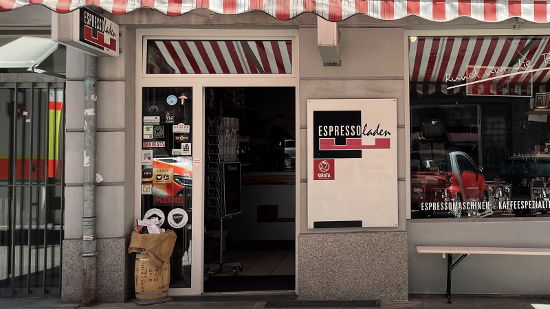Espresso store in Stuttgart-Süd with red and white striped awning, shop window and entrance door. Stickers and coffee bags are visible., © Espressoladen, Stuttgart