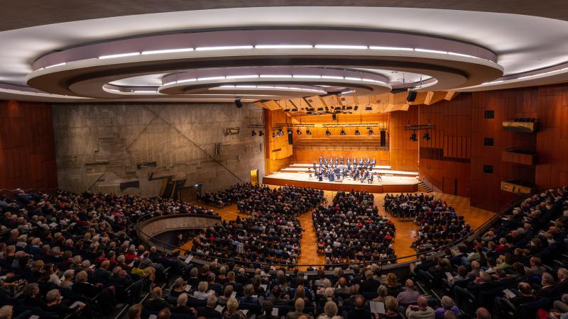 Ein gro&szlig;er Konzertsaal mit modernem Design, gef&uuml;llt mit Zuschauern. Auf der B&uuml;hne spielt ein Orchester. Die Architektur ist beeindruckend., &copy; Holger Schneider